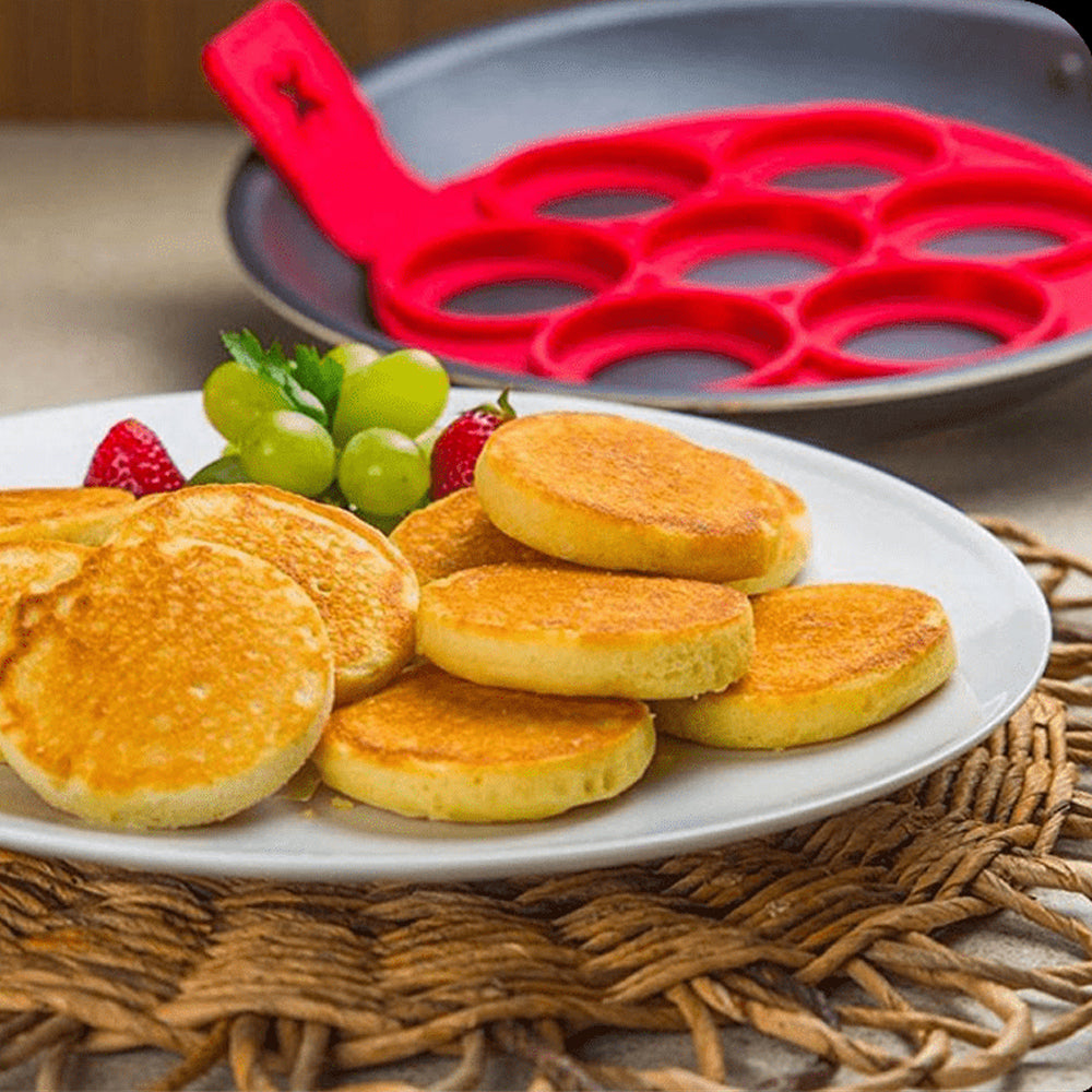 Teller mit kleinen Pfannkuchen und roten Früchten, dahinter rote Silikonform in grauer Pfanne
